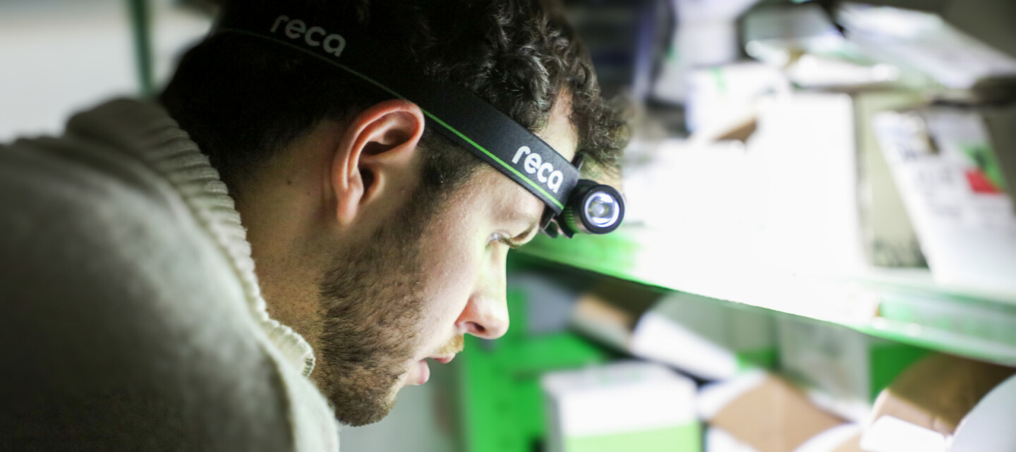Pracovník s čelovkou RECA ze speciální edice při kontrole zboží na regálech ve skladu.